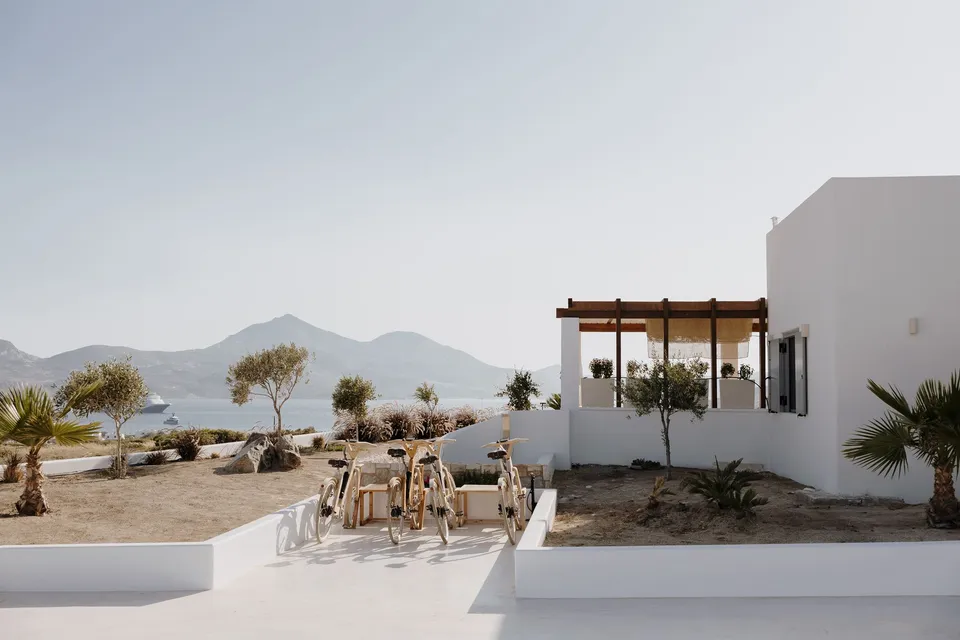 The white villa terrace with dining chairs, a timber pergola and views towards the sea, at Adriana Luxury Villas on Milos, Greece, during an Elopement Collective elopement. Photograph by George Bowden.