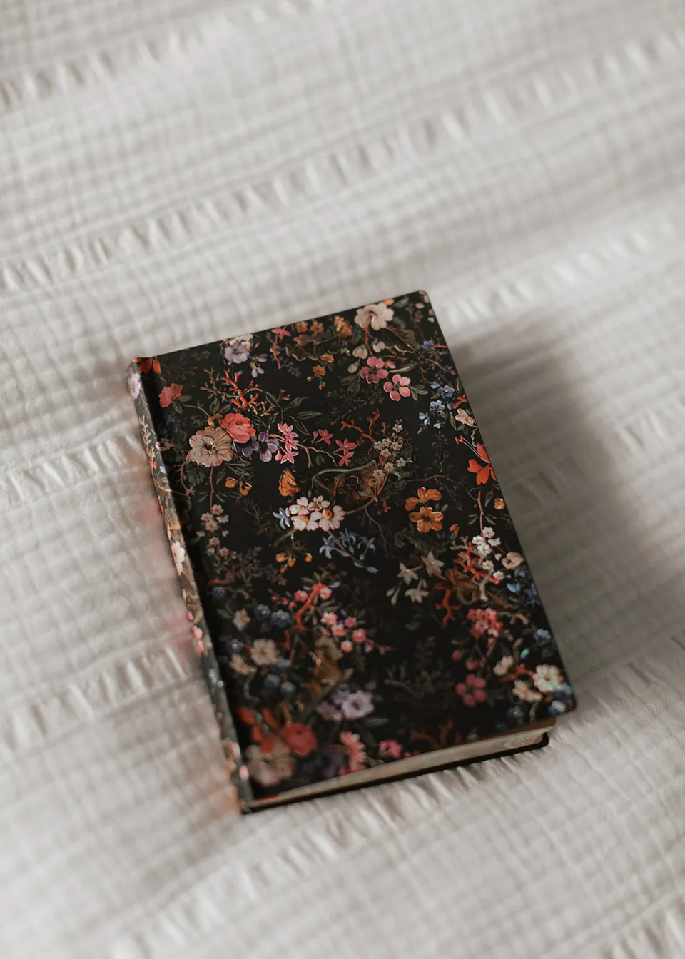 A dark floral-patterned booklet resting on a white bedspread. At Fig Tree Villa in Ewingsdale, Byron Bay, for an Elopement Collective elopement. Photograph by Bulb Creative.