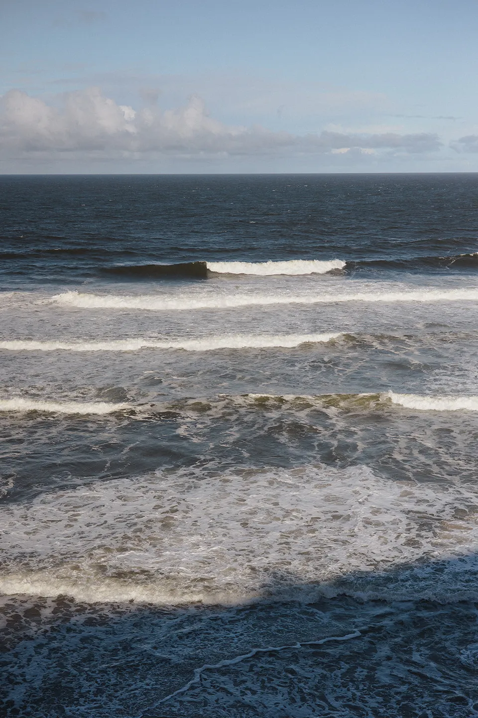 Waves rolling towards the sand at Whites Beach beneath a pale blue sky. At Whites Beach, Broken Head, near Byron Bay, for an Elopement Collective elopement. Photograph by Jason Lucas.