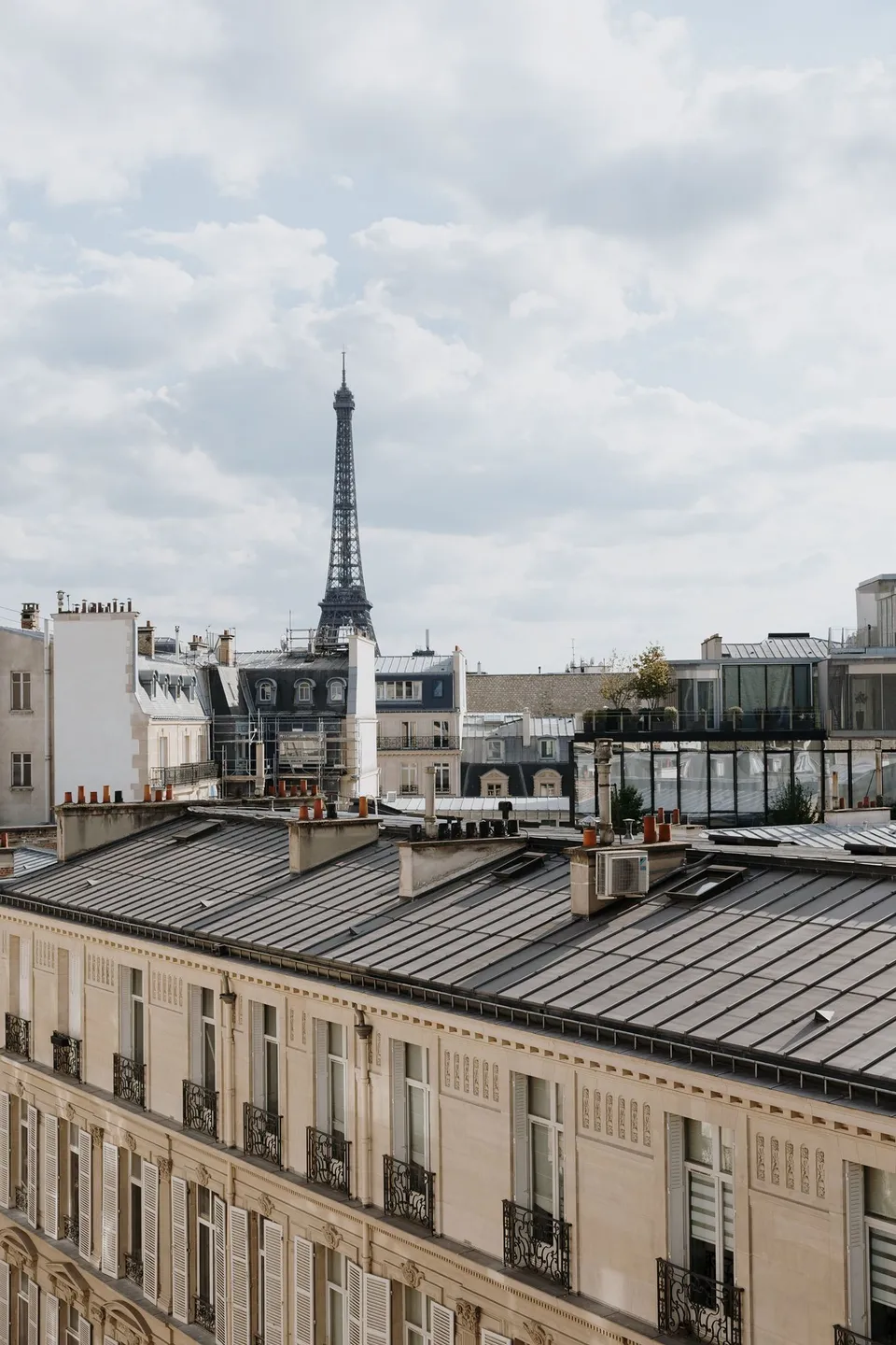 The Eiffel Tower rising beyond slate-roofed Parisian buildings beneath a partly cloudy sky, at Hotel Marignan Champs-Élysées in Paris, France, during an Elopement Collective elopement. Photograph by George Bowden.