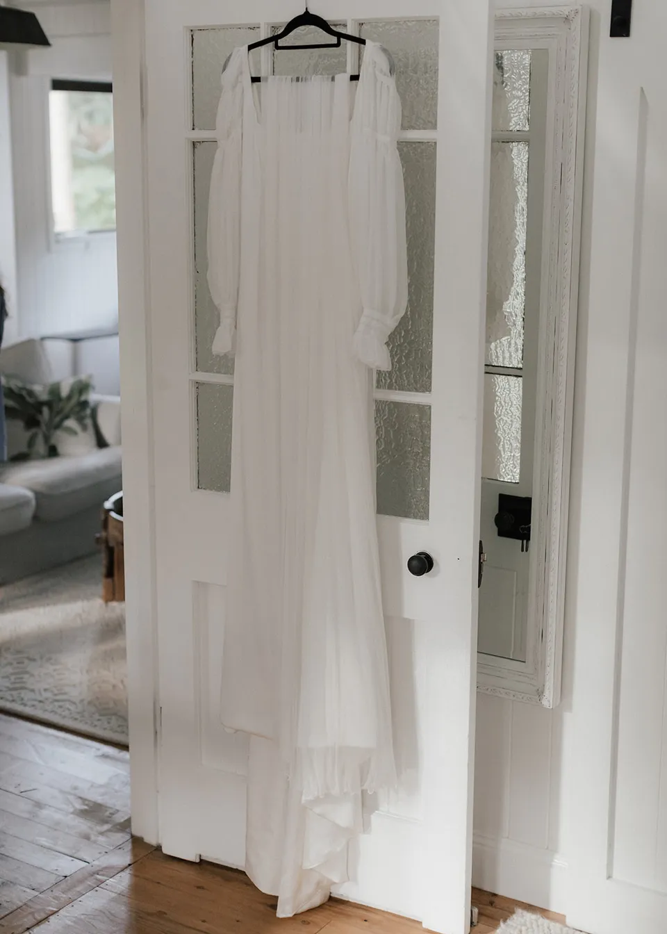 Elyse's long white wedding dress hanging from the bedroom doorway. At Fig Tree Villa in Ewingsdale, Byron Bay, for an Elopement Collective elopement. Photograph by Bulb Creative.