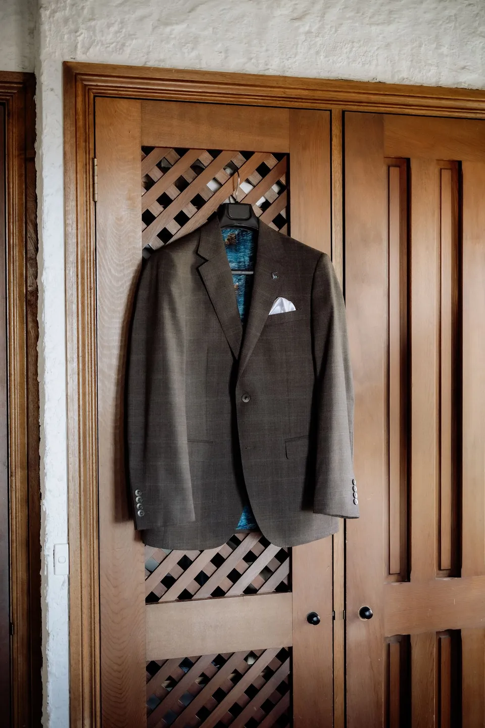 Russell’s checked brown suit jacket hanging on a timber wardrobe inside the cottage. At Piermont Retreat on Tasmania’s east coast, for an Elopement Collective elopement. Photograph by Omar of By The Wilde.
