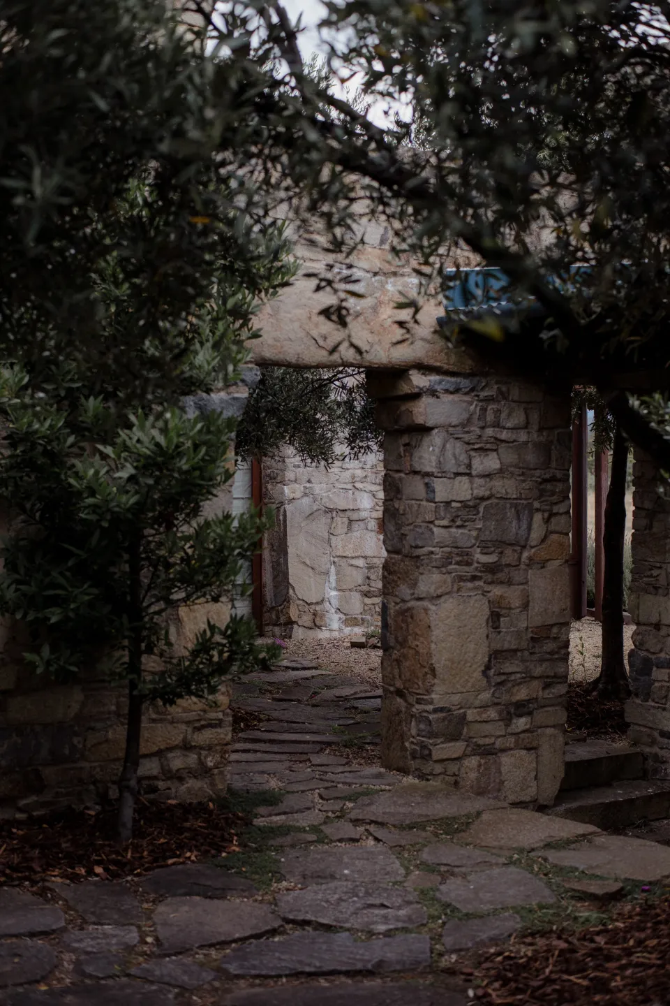 A shaded stone courtyard beneath leafy branches, at Thalia Haven on the East Coast of Tasmania, Australia, for an Elopement Collective elopement. Photograph by Joey Willis.