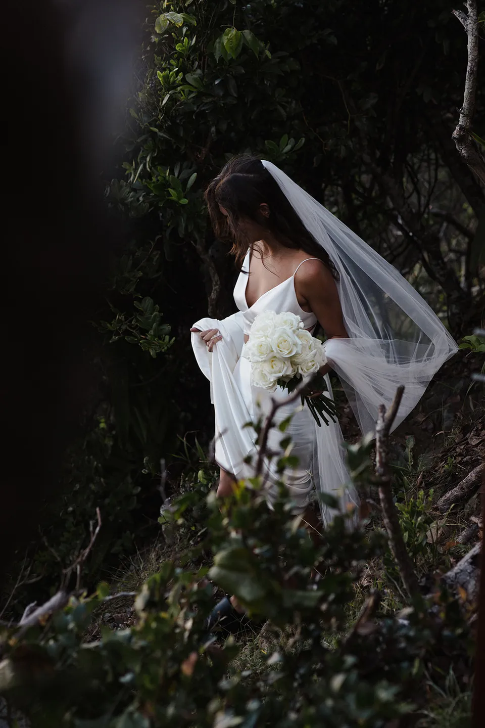 Rachel lifting her dress as her veil catches the breeze on the forest path. At Whites Beach, Broken Head, near Byron Bay, for an Elopement Collective elopement. Photograph by Jason Lucas.
