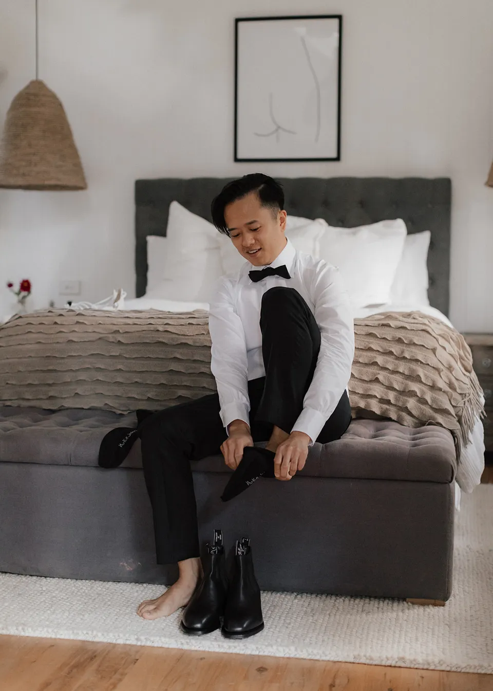Jonathan putting on his socks while seated at the end of the bed. At Fig Tree Villa in Ewingsdale, Byron Bay, for an Elopement Collective elopement. Photograph by Bulb Creative.