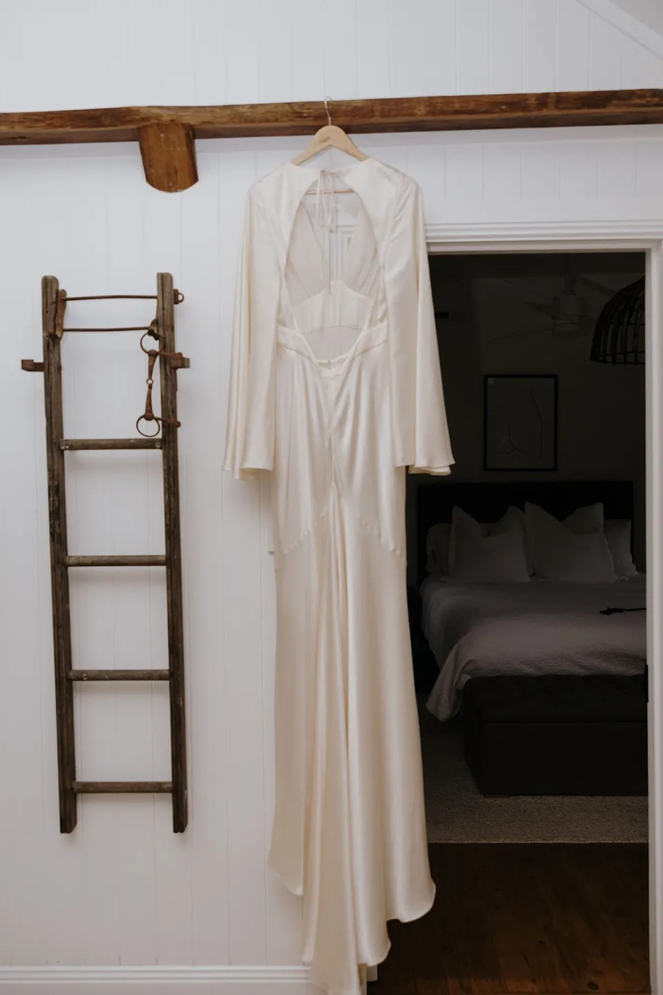 Laura's flowing wedding dress hanging from a timber beam inside the villa. At Fig Tree Villa in Ewingsdale, Byron Bay, for an Elopement Collective elopement. Photograph by George Bowden.