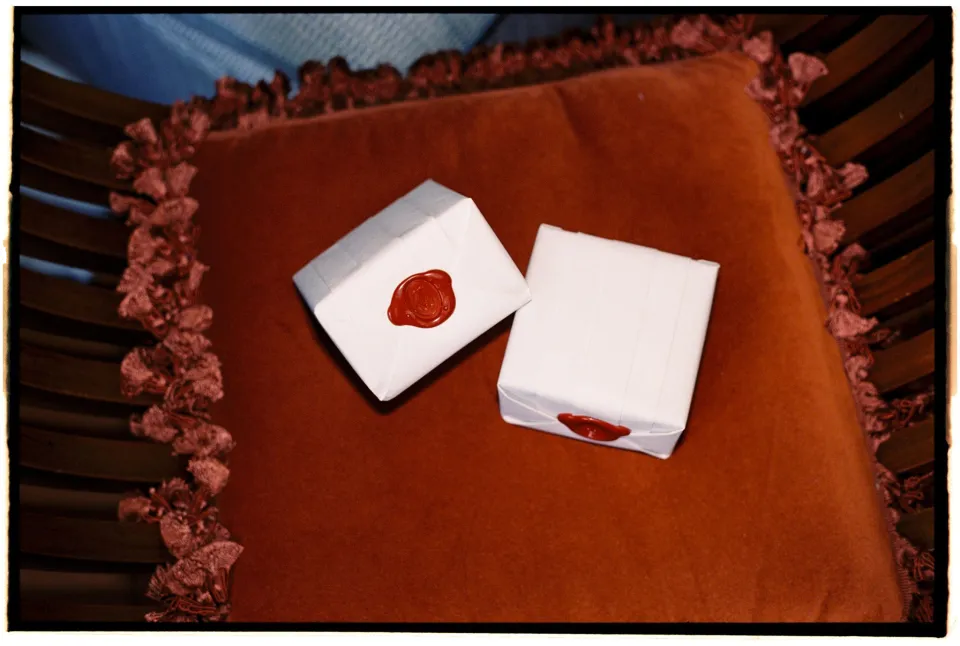 Folded wedding stationery and a red wax-sealed envelope on an orange upholstered chair, at Villa San Michele in Fiesole above Florence, Tuscany, Italy, for an Elopement Collective elopement. Film photograph by Khara from House of Lucie.