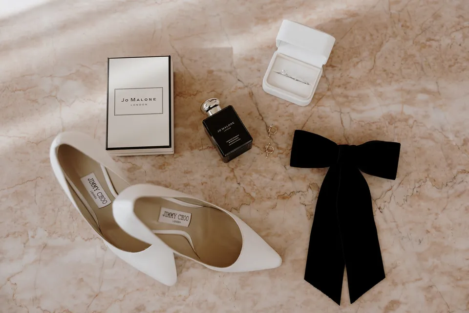 White pointed heels, perfume, a jewellery box and a black ribbon bow on pink stone, at The Calile Hotel in Fortitude Valley, Brisbane, for an Elopement Collective elopement. Photo by George Bowden.