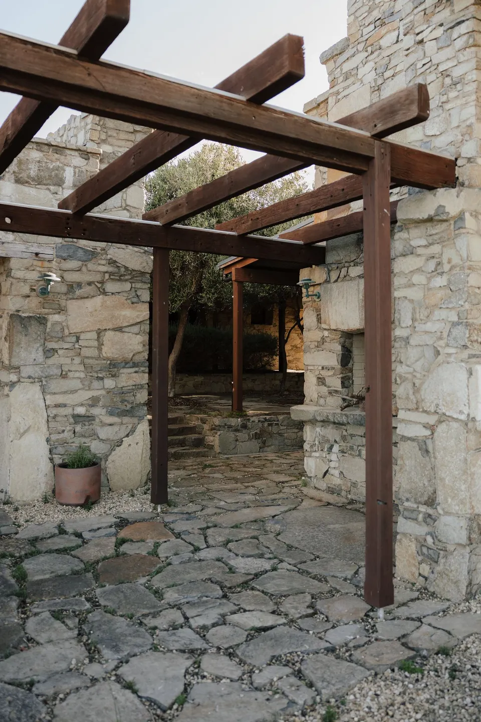 Stone paving and walls beneath a timber pergola in Thalia Haven’s courtyard, at Thalia Haven on the East Coast of Tasmania, for an Elopement Collective elopement. Photograph by Bulb Creative.