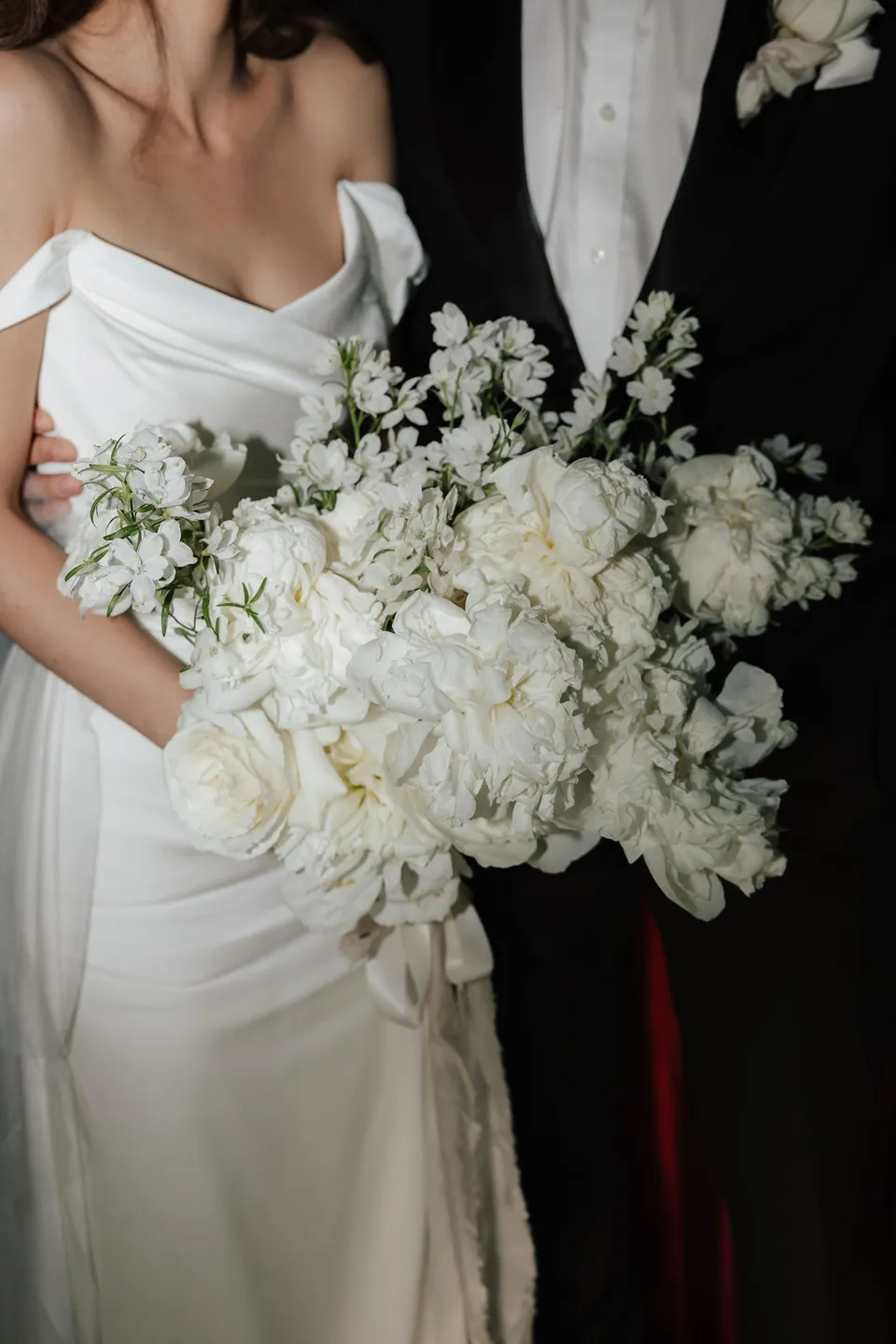 Clara’s white bouquet by The Romantics against her draped white dress and Harry’s black tuxedo and white buttonhole, at Thalia Haven on the East Coast of Tasmania, for an Elopement Collective elopement. Photograph by Bulb Creative.