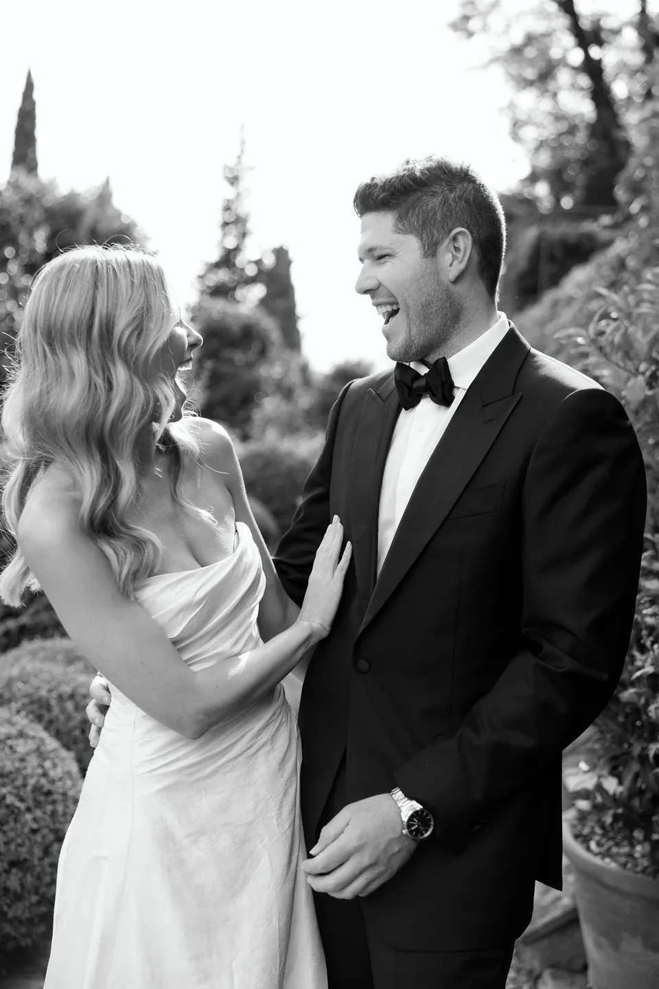 Black-and-white portrait of Holly and Matthew laughing together in the garden; Holly’s loose waves and bridal makeup by Shannon Hope are visible, at Villa San Michele in Fiesole above Florence, Tuscany, Italy, for an Elopement Collective elopement. Digital photograph by Khara from House of Lucie.