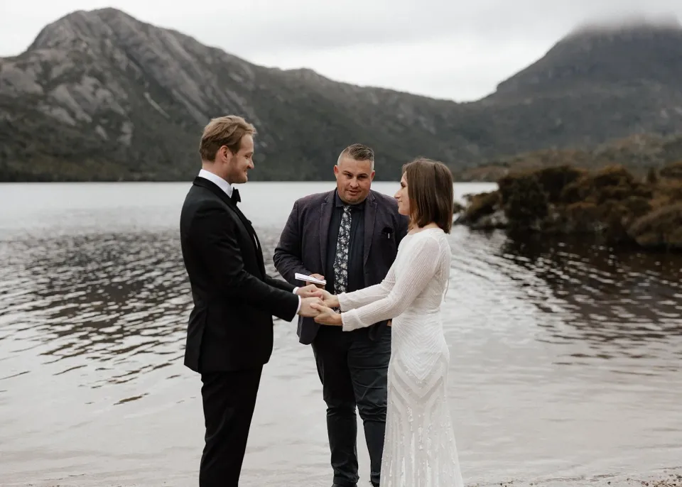 April and Josh holding hands during their ceremony with celebrant Josh Withers, at Dove Lake, Cradle Mountain, Tasmania, for an Elopement Collective elopement. Photo by Bulb Creative.