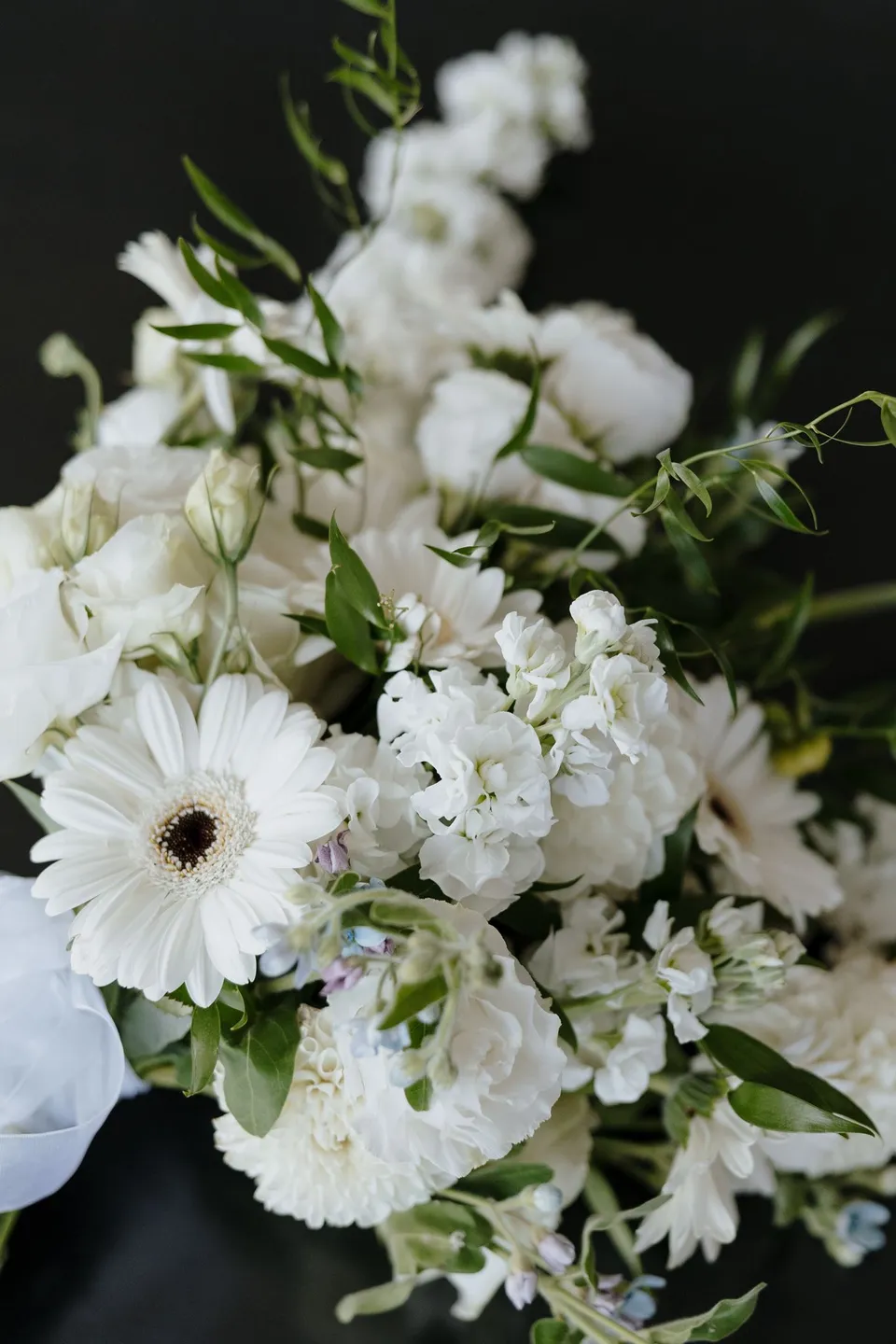 A close-up of the Orange Blossom bouquet with white daisy-like flowers, pale blooms and trailing greenery, at their Airbnb in Fernhill, Queenstown, New Zealand, for an Elopement Collective Queenstown elopement. Photo by George Bowden.