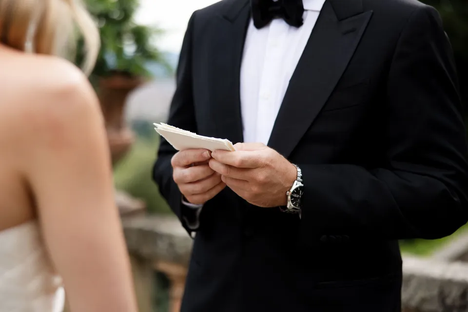 Close view of Matthew’s hands holding his vow card beneath his black bow tie, at Villa San Michele in Fiesole above Florence, Tuscany, Italy, for an Elopement Collective elopement. Digital photograph by Khara from House of Lucie.