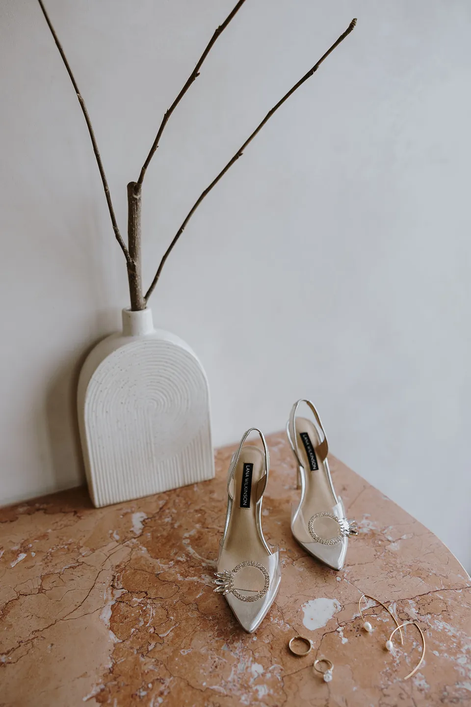 Gabrielle’s pointed Lana Wilkinson slingback heels and jewellery on a stone table beside a white vase, at Roundhill Retreat in Obi Obi, Sunshine Coast Hinterland, Queensland, for an Elopement Collective elopement. Photo by George Bowden.