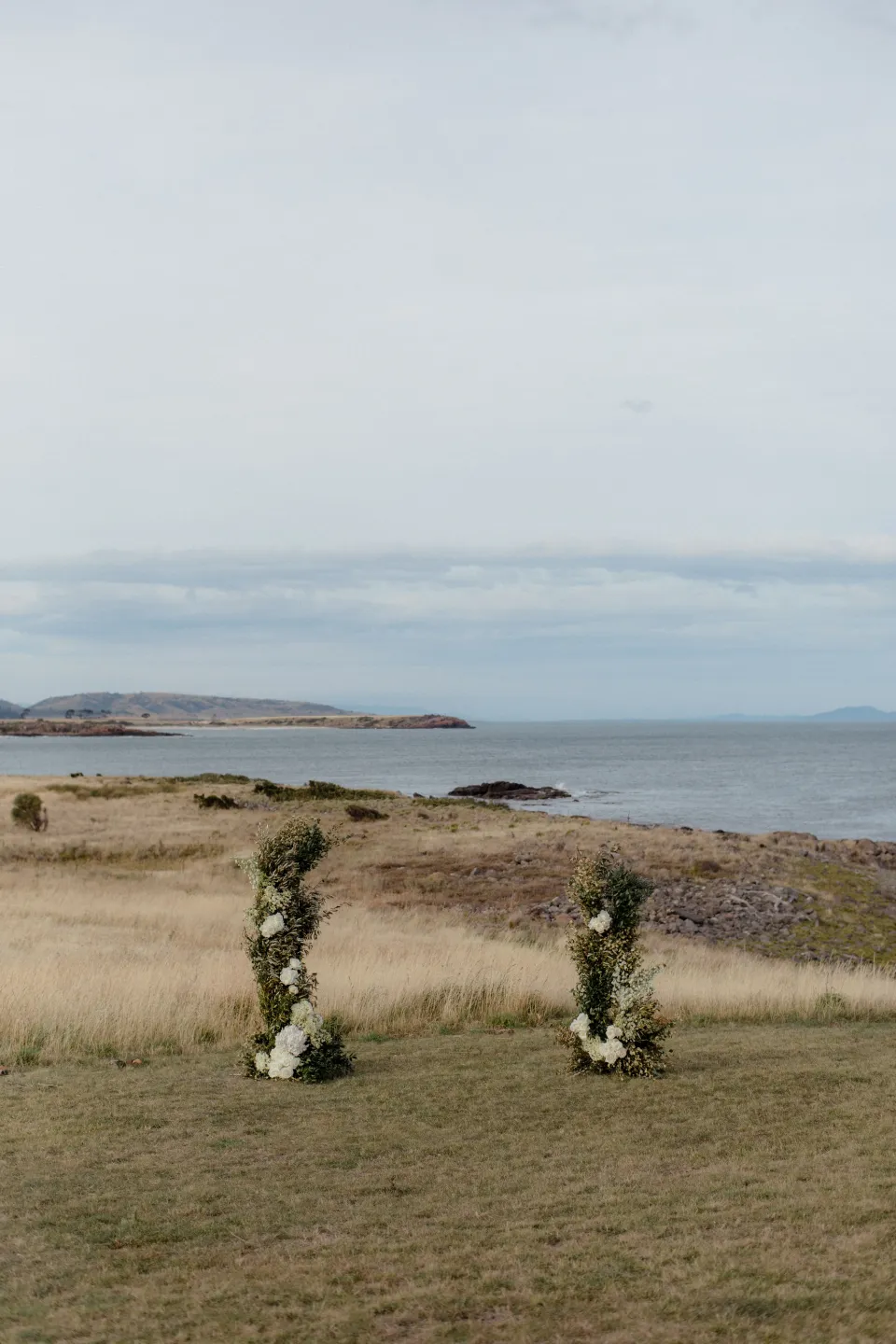 Two ceremony flower arrangements by The Romantics on the lawn above the bay, at Thalia Haven on the East Coast of Tasmania, Australia, for the Elopement Collective elopement. Photograph by Joey Willis.
