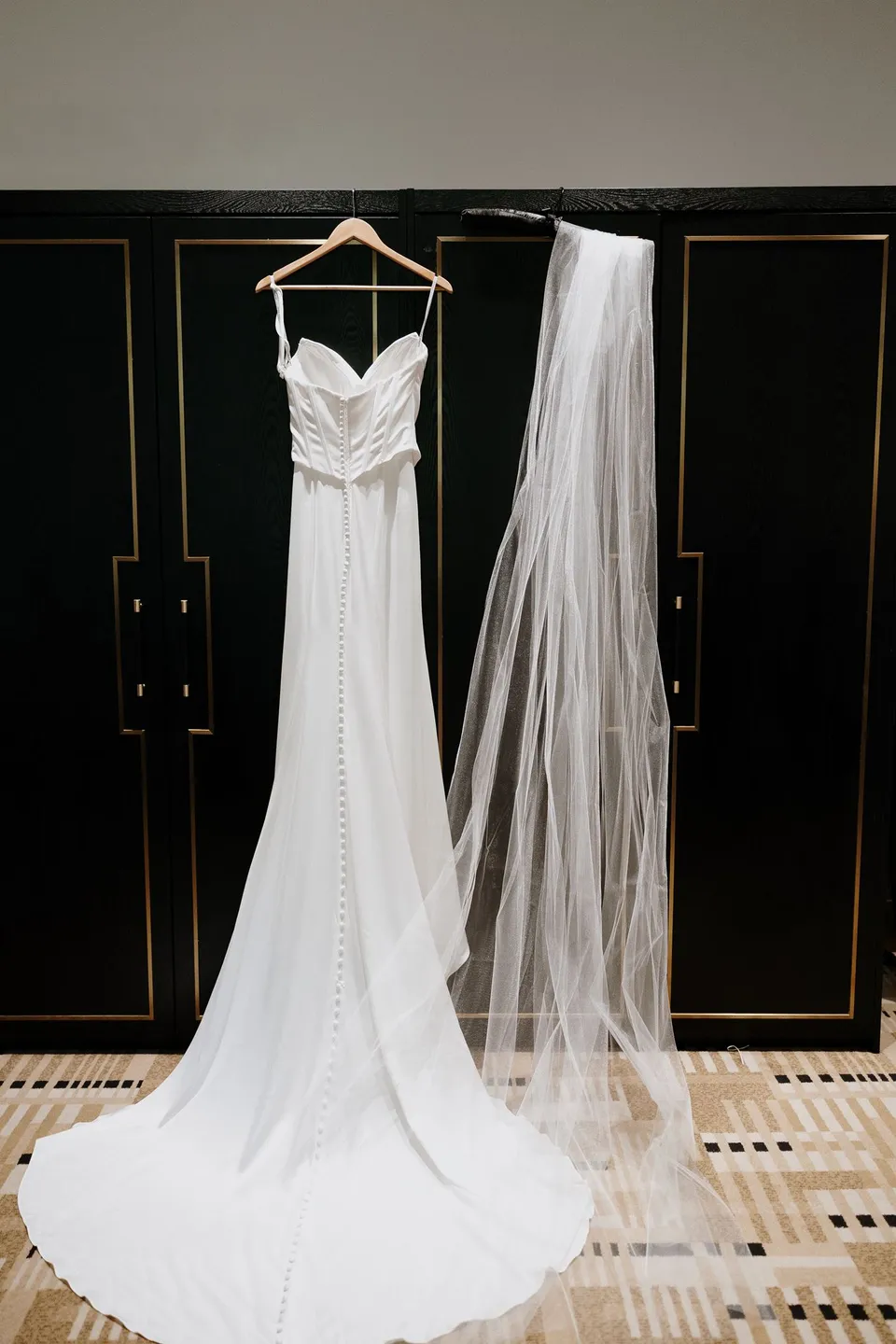 Tanesha’s white wedding dress and long veil hanging against a dark wardrobe in her hotel room, at Islington Hotel in South Hobart, Tasmania, Australia, for an Elopement Collective summer elopement. Photograph by George Bowden.