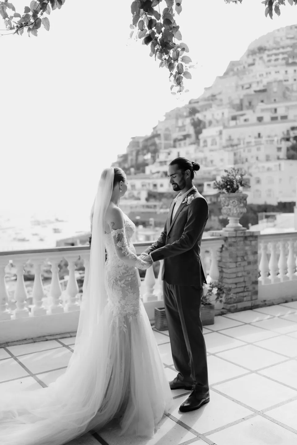 Black and white photograph of Skyler and Zach facing each other beside the terrace balustrade during their ceremony, at Hotel Buca di Bacco in Positano, Amalfi Coast, Italy, for an Elopement Collective elopement. Photograph by Jason Corroto.