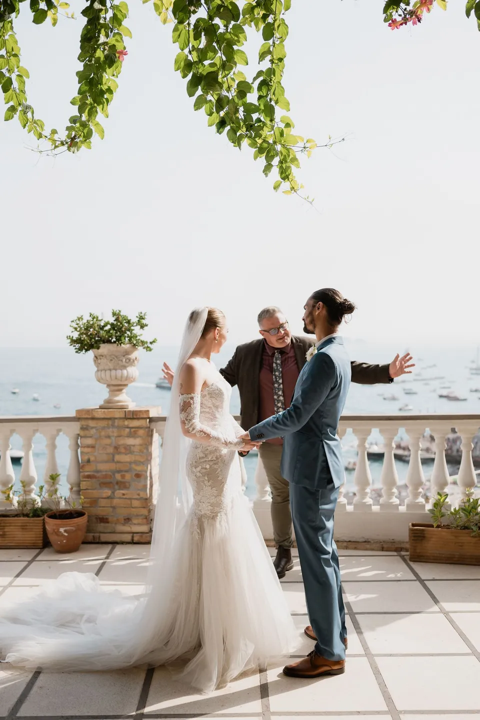 Celebrant Josh Withers speaking as Skyler and Zach face each other on the hotel terrace, at Hotel Buca di Bacco in Positano, Amalfi Coast, Italy, for an Elopement Collective elopement. Photograph by Jason Corroto.