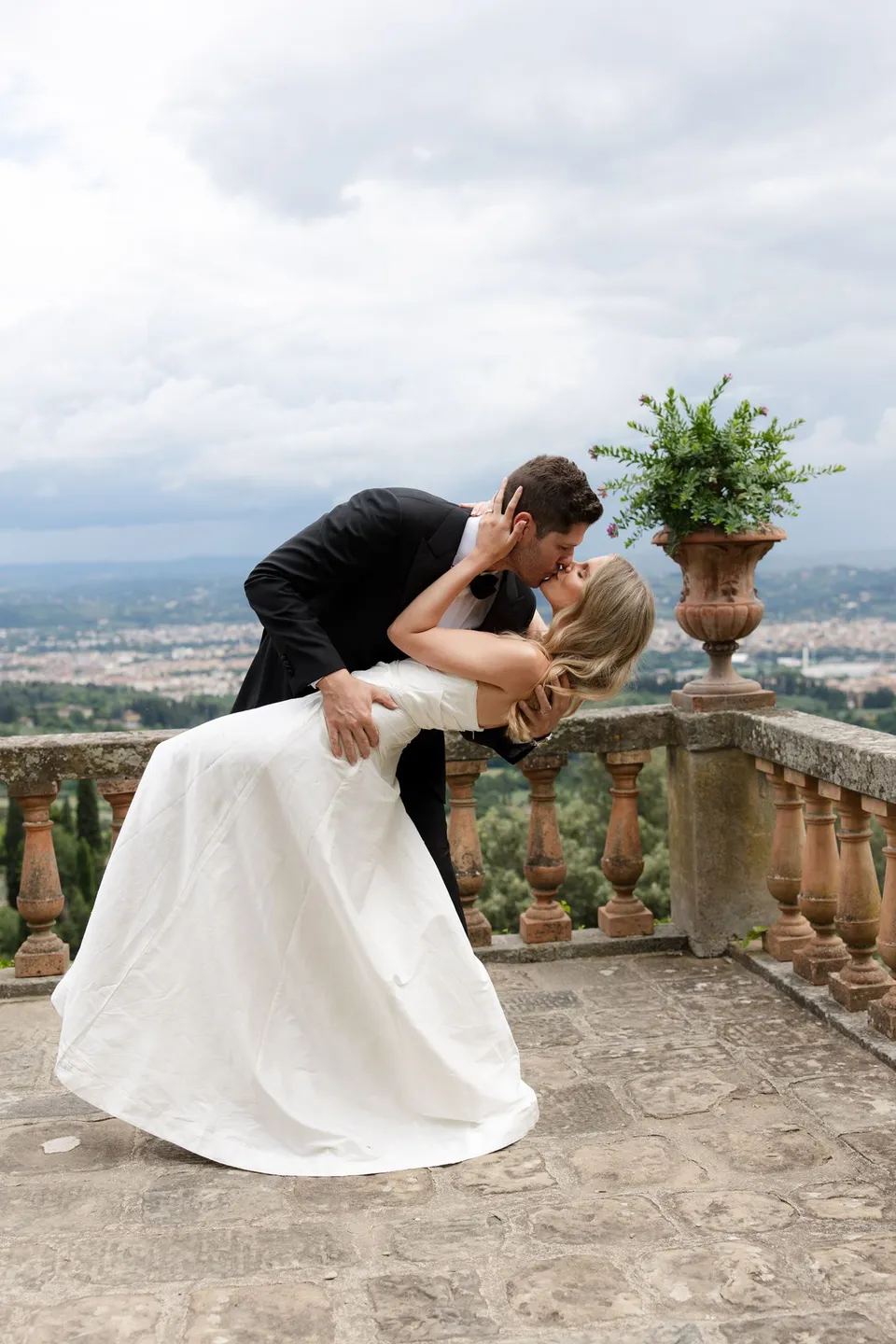 Matthew dipping Holly into a kiss on the stone terrace overlooking Florence, at Villa San Michele in Fiesole above Florence, Tuscany, Italy, for an Elopement Collective elopement. Digital photograph by Khara from House of Lucie.