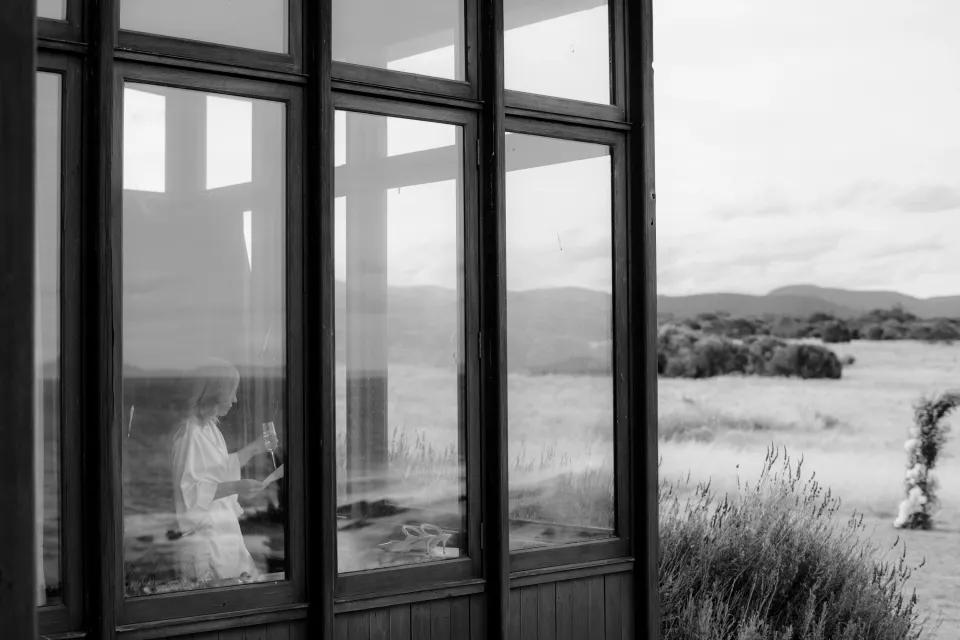 Black and white view through the house windows towards the coastal grounds, at Thalia Haven on the East Coast of Tasmania, Australia, for an Elopement Collective elopement. Photograph by Joey Willis.