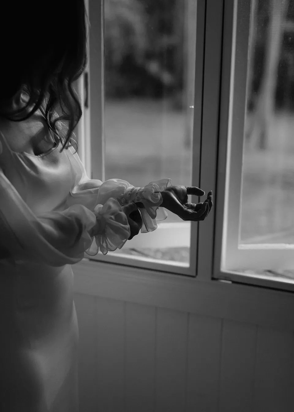 Black-and-white detail of Elyse adjusting her sleeve in the window light. At Fig Tree Villa in Ewingsdale, Byron Bay, for an Elopement Collective elopement. Photograph by Bulb Creative.