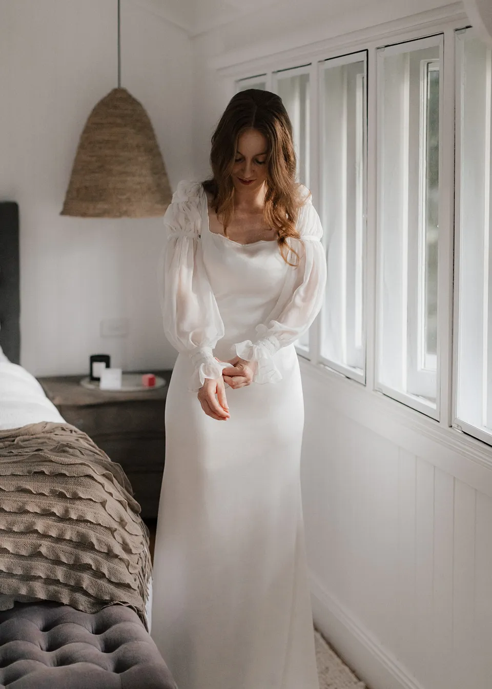 Elyse standing by the bedroom window in her wedding dress. At Fig Tree Villa in Ewingsdale, Byron Bay, for an Elopement Collective elopement. Photograph by Bulb Creative.