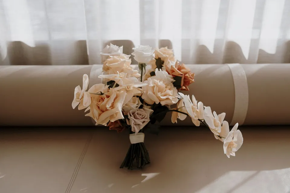 Danielle’s bouquet of peach and white flowers with trailing orchids by Mrs Gibbons Florals resting on a pale sofa, at The Calile Hotel in Fortitude Valley, Brisbane, for an Elopement Collective elopement. Photo by George Bowden.