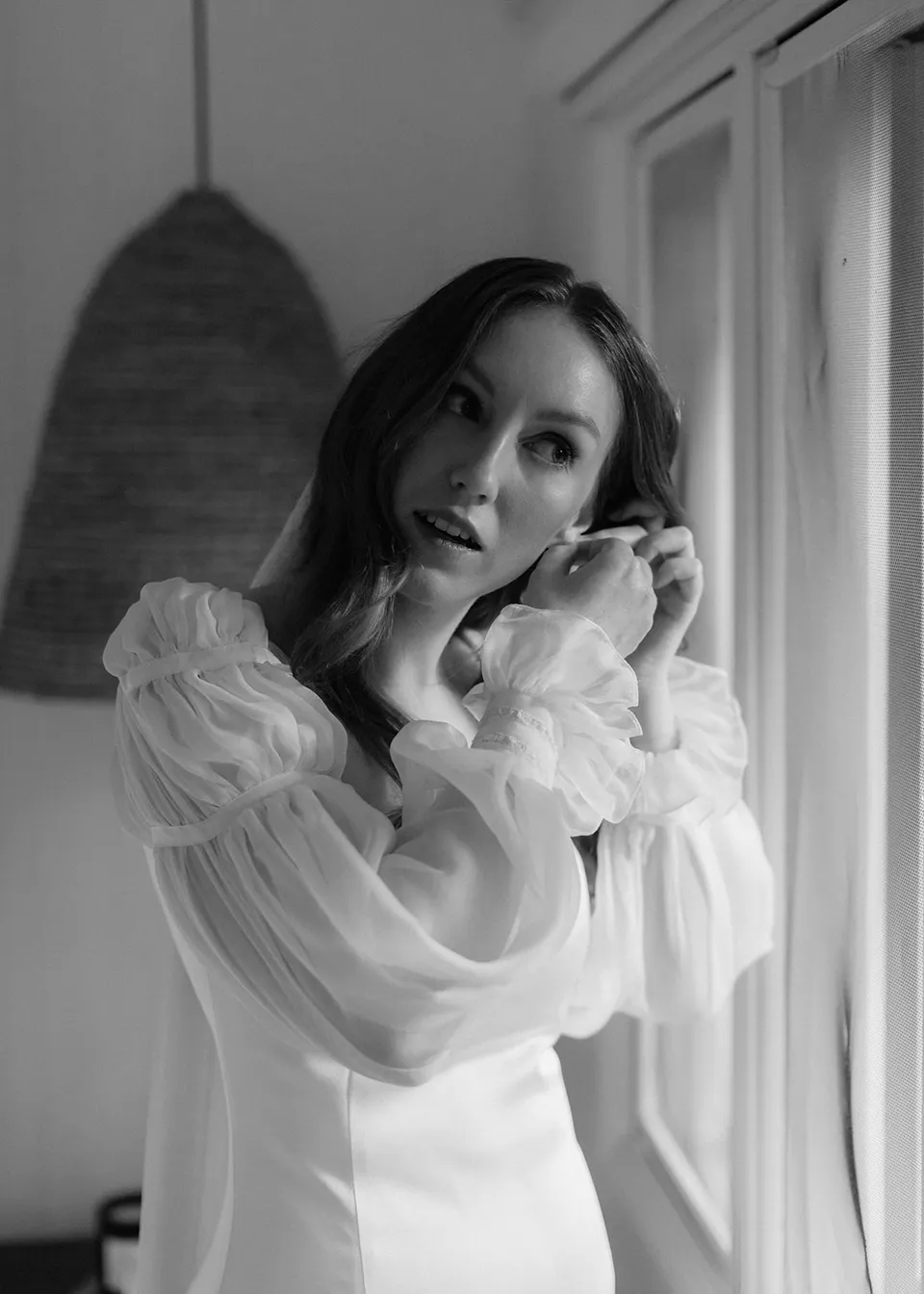 Black-and-white portrait of Elyse putting on an earring. At Fig Tree Villa in Ewingsdale, Byron Bay, for an Elopement Collective elopement. Photograph by Bulb Creative.