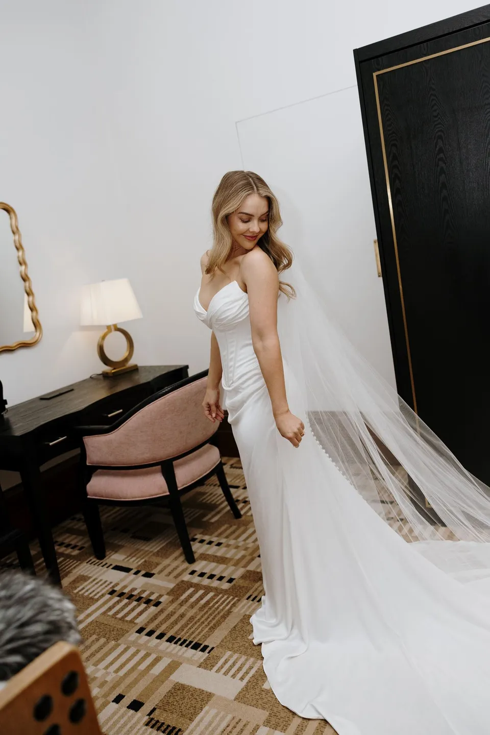 Tanesha looking back over her shoulder in her wedding dress, with her veil trailing beside a writing desk, at Islington Hotel in South Hobart, Tasmania, Australia, for an Elopement Collective summer elopement. Photograph by George Bowden.