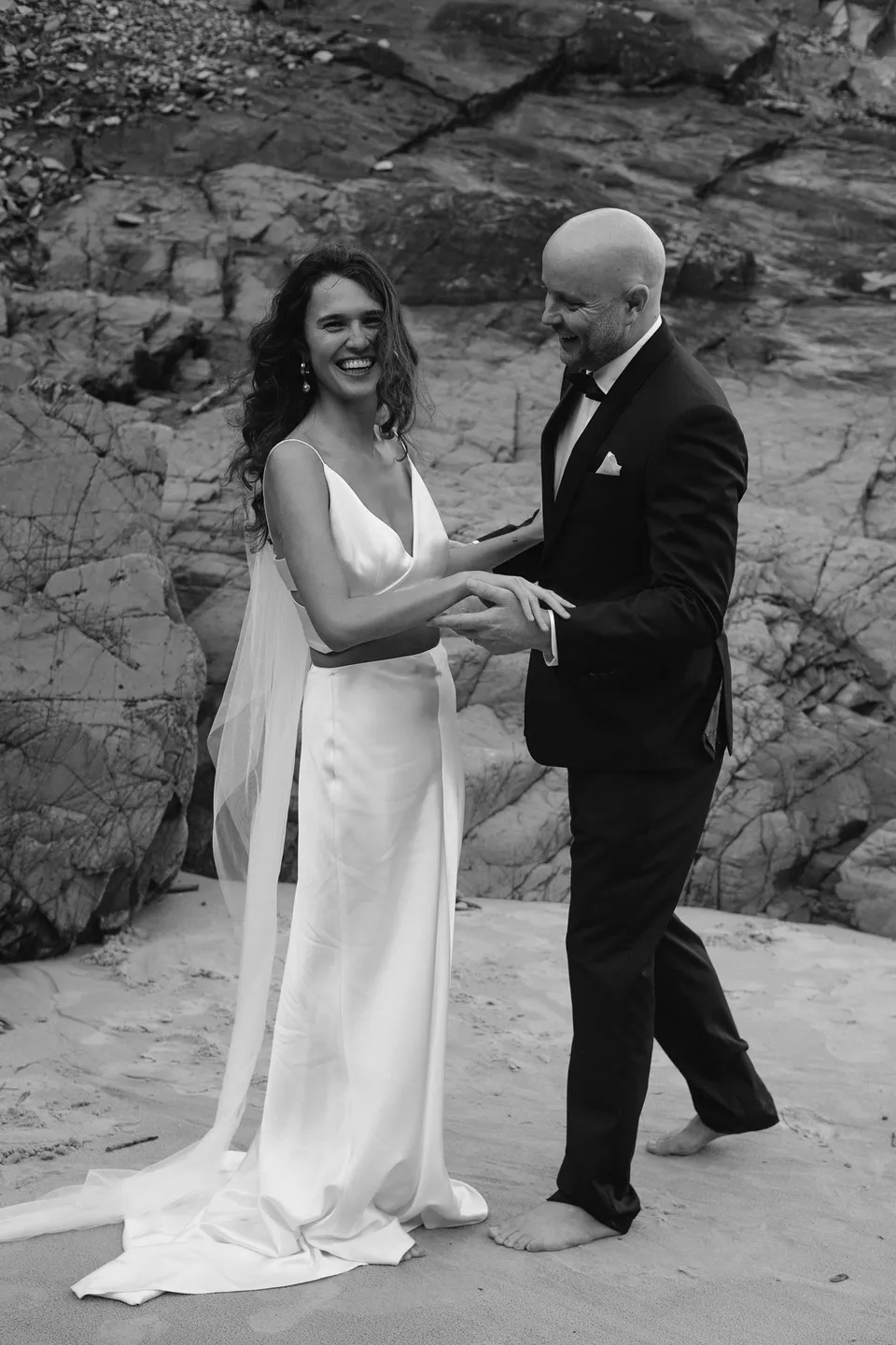 Black-and-white photograph of Rachel and Dane laughing together after their ceremony. At Whites Beach, Broken Head, near Byron Bay, for an Elopement Collective elopement. Photograph by Jason Lucas.