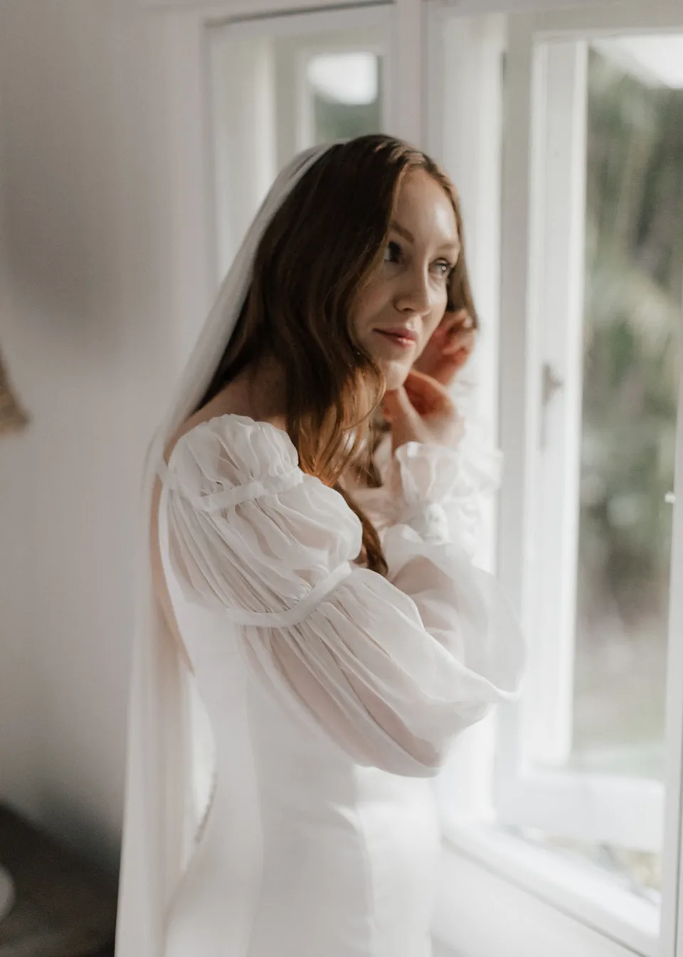 Close portrait of Elyse adjusting her earring beside the open window. At Fig Tree Villa in Ewingsdale, Byron Bay, for an Elopement Collective elopement. Photograph by Bulb Creative.