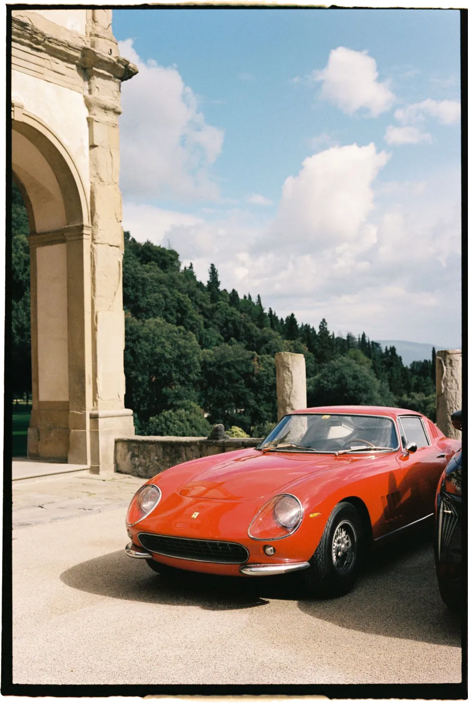 A red vintage sports car beside the villa’s stone cloister and garden shrubs, at Villa San Michele in Fiesole above Florence, Tuscany, Italy, for an Elopement Collective elopement. Film photograph by Khara from House of Lucie.