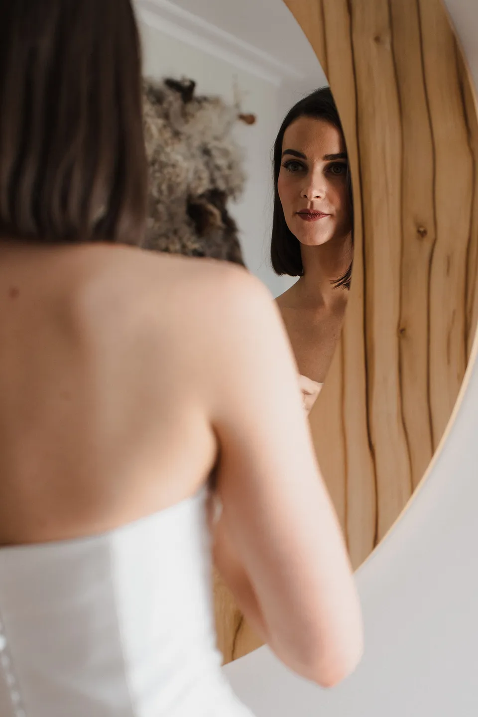 Meg’s reflection in a round timber mirror as she gets ready in her strapless wedding dress. At The Keep on Tasmania’s east coast, for an Elopement Collective elopement. Photograph by Jenna Agius.