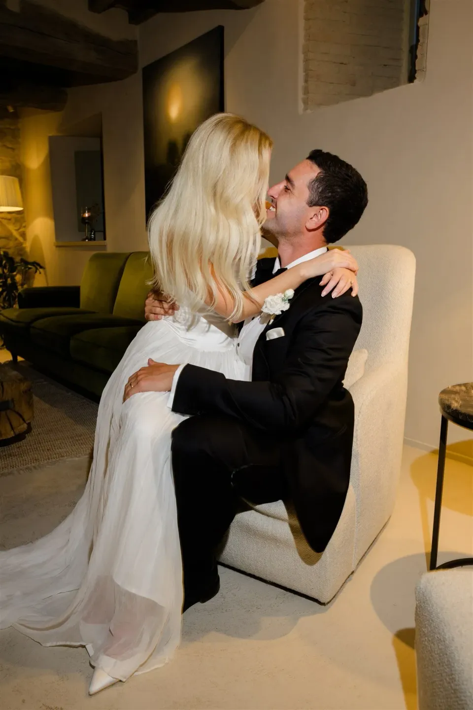 Shelby and Jack kissing as she sits on his lap in a cream armchair, in Umbria, Italy, for an Elopement Collective elopement. Photo by James from House of Love.