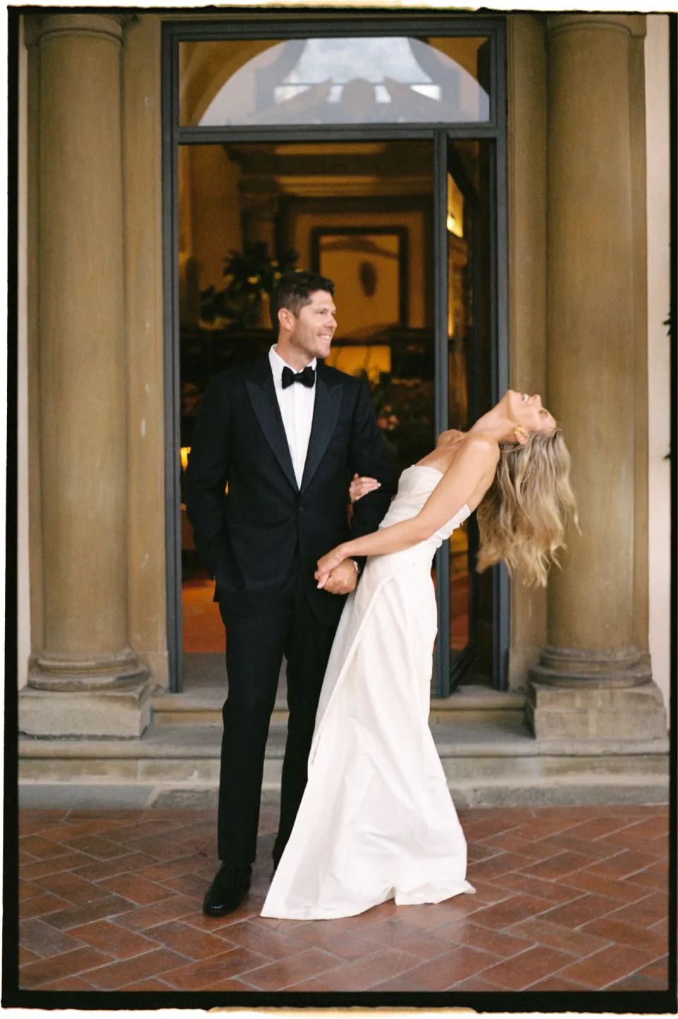 Holly leaning back laughing beside Matthew in the villa’s stone doorway, at Villa San Michele in Fiesole above Florence, Tuscany, Italy, for an Elopement Collective elopement. Film photograph by Khara from House of Lucie.