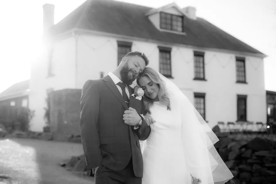Black and white portrait of Kaitlyn and Russell leaning their heads together outside the homestead. At Piermont Retreat on Tasmania’s east coast, for an Elopement Collective elopement. Photograph by Omar of By The Wilde.