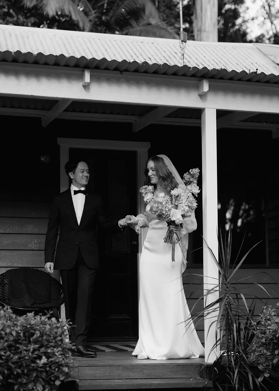 Black-and-white photograph of Elyse and Jonathan together on the cottage verandah. At Fig Tree Villa in Ewingsdale, Byron Bay, for an Elopement Collective elopement. Photograph by Bulb Creative.