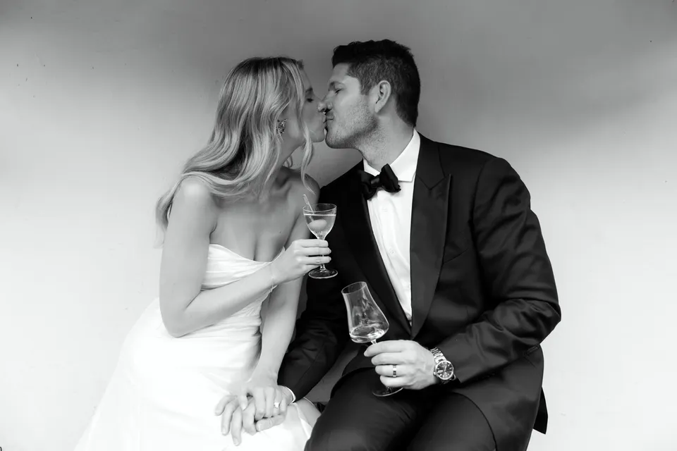 Black-and-white photograph of Holly and Matthew kissing on the sofa with their wine glasses, at Villa San Michele in Fiesole above Florence, Tuscany, Italy, for an Elopement Collective elopement. Digital photograph by Khara from House of Lucie.