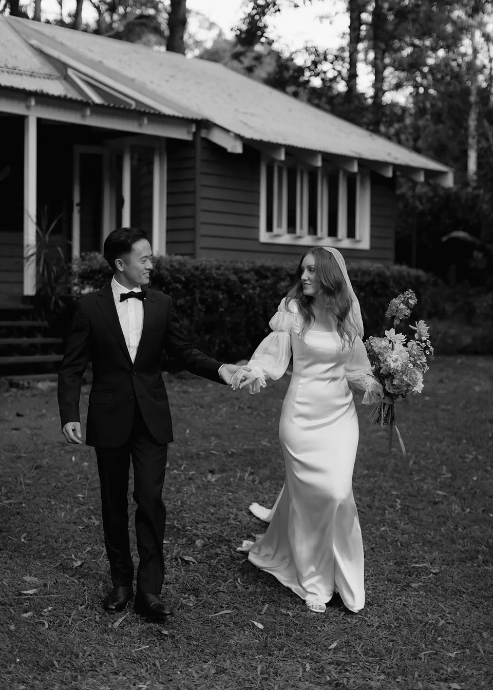 Black-and-white photograph of Elyse and Jonathan walking away from the verandah. At Fig Tree Villa in Ewingsdale, Byron Bay, for an Elopement Collective elopement. Photograph by Bulb Creative.