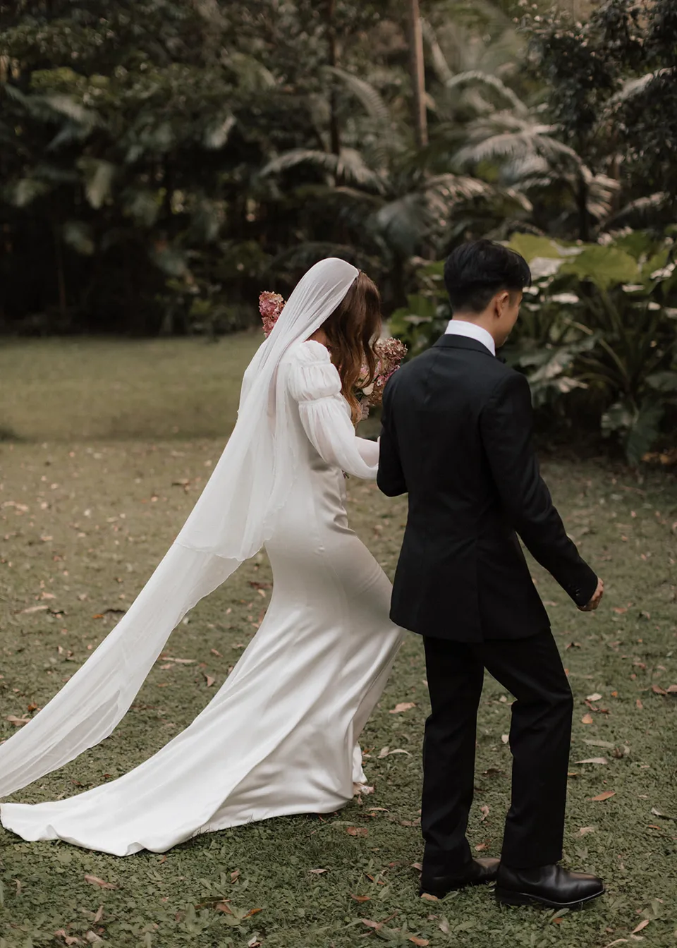 Rear view of Elyse and Jonathan approaching their garden ceremony. At Fig Tree Villa in Ewingsdale, Byron Bay, for an Elopement Collective elopement. Photograph by Bulb Creative.
