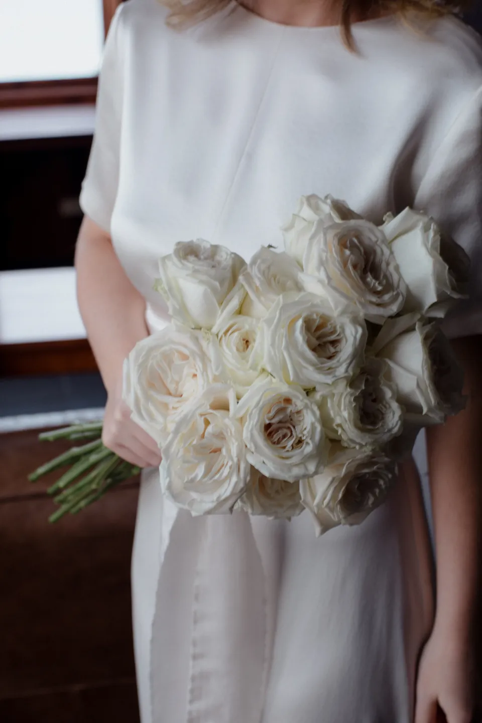 A close view of Jemmah’s white rose bouquet by The Romantics against her dress, at Thalia Haven on the East Coast of Tasmania, Australia, for an Elopement Collective elopement. Photograph by Joey Willis.
