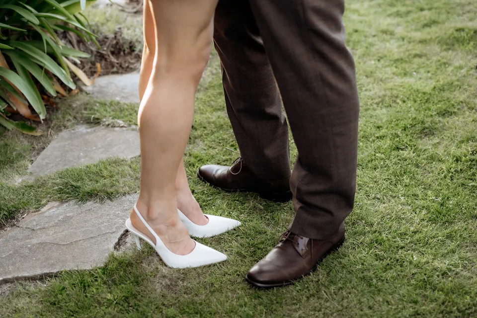 Close-up of Kaitlyn’s white slingback shoes and Russell’s brown shoes on the lawn beside a stone path. At Piermont Retreat on Tasmania’s east coast, for an Elopement Collective elopement. Photograph by Omar of By The Wilde.