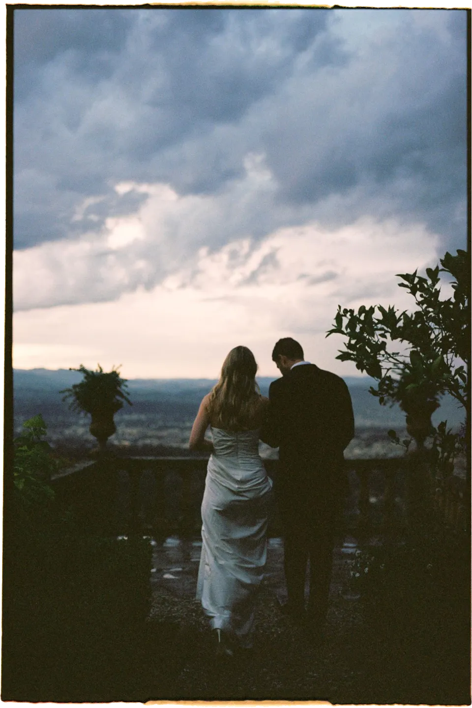Holly and Matthew looking out across Florence as the light fades beneath a cloudy sky, at Villa San Michele in Fiesole above Florence, Tuscany, Italy, for an Elopement Collective elopement. Film photograph by Khara from House of Lucie.