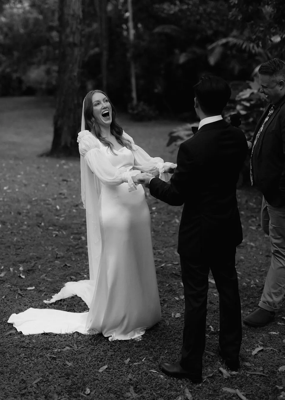 Black-and-white photograph of Elyse laughing with Jonathan in the garden. At Fig Tree Villa in Ewingsdale, Byron Bay, for an Elopement Collective elopement. Photograph by Bulb Creative.