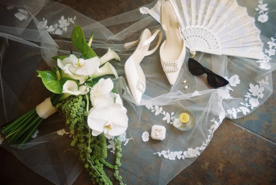 White calla lilies, heart-shaped white blooms and trailing greenery by Garden of Love arranged with an embroidered veil, pleated fan, shoes and jewellery, at Lake Como in Lombardy, Italy, for an Elopement Collective elopement. Photograph by George Bowden.
