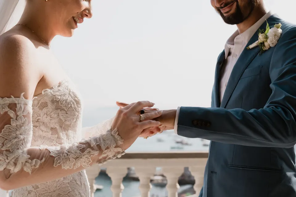 Close view of Skyler placing a wedding ring on Zach’s finger during their terrace ceremony, at Hotel Buca di Bacco in Positano, Amalfi Coast, Italy, for an Elopement Collective elopement. Photograph by Jason Corroto.