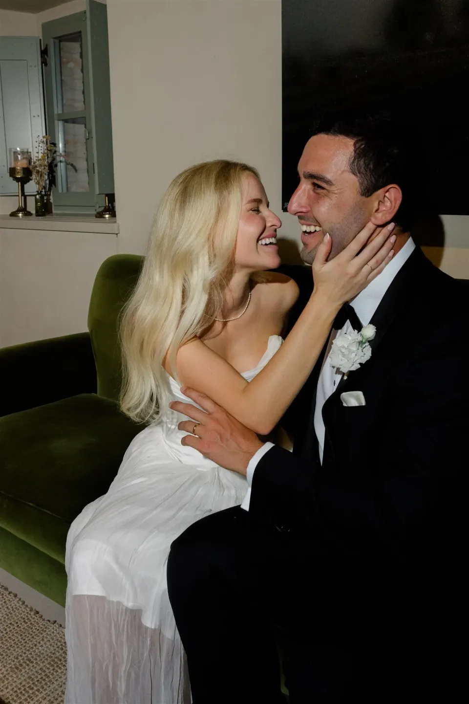 Shelby sitting on Jack’s lap beside a green sofa as they smile at one another, in Umbria, Italy, for an Elopement Collective elopement. Photo by James from House of Love.