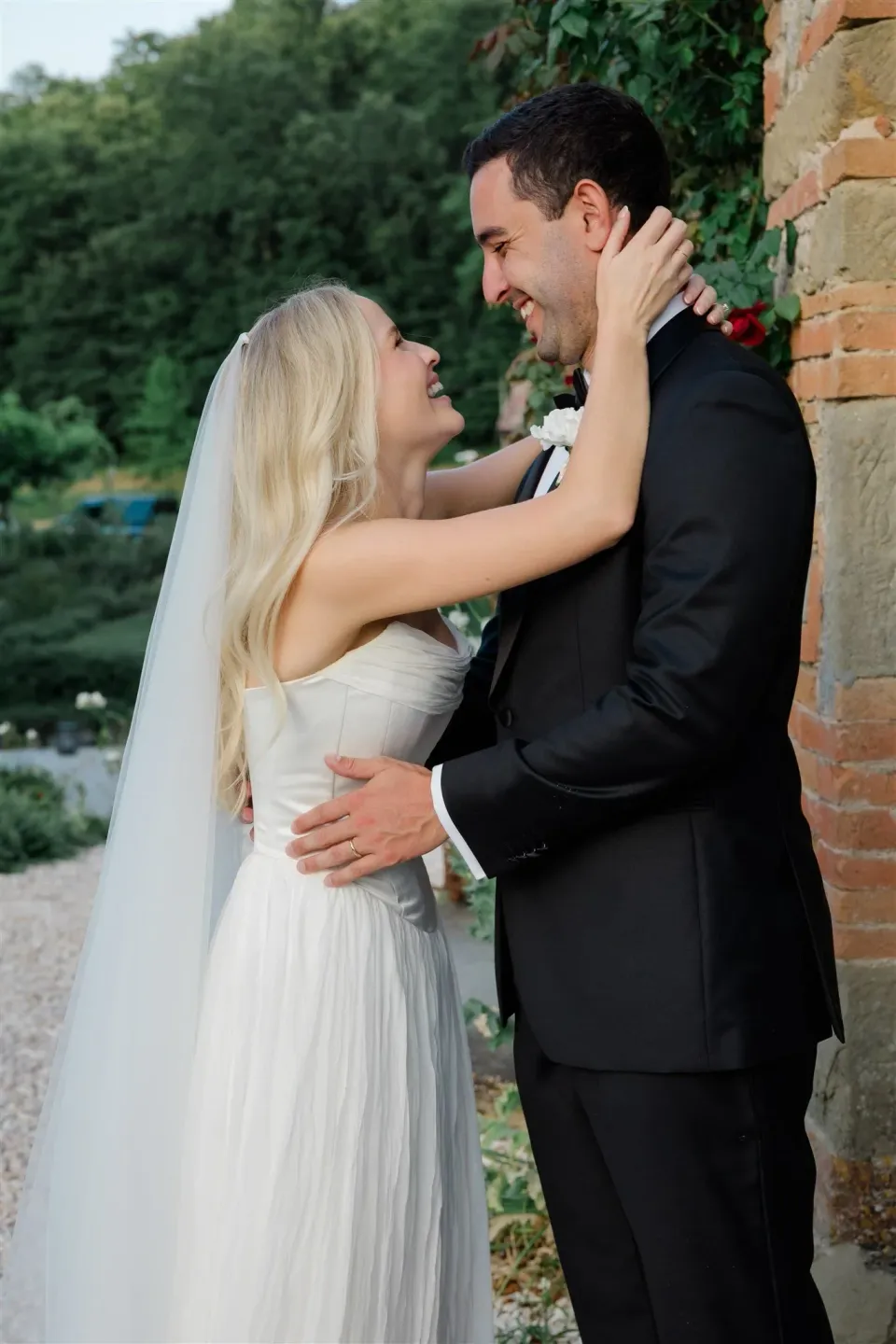 Shelby resting her hands around Jack’s face as they smile together beside a brick doorway, in Umbria, Italy, for an Elopement Collective elopement. Photo by James from House of Love.