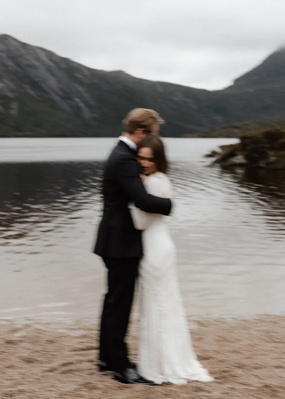 Softly blurred portrait of April and Josh embracing beside the lake, at Dove Lake, Cradle Mountain, Tasmania, for an Elopement Collective elopement. Photo by Bulb Creative.